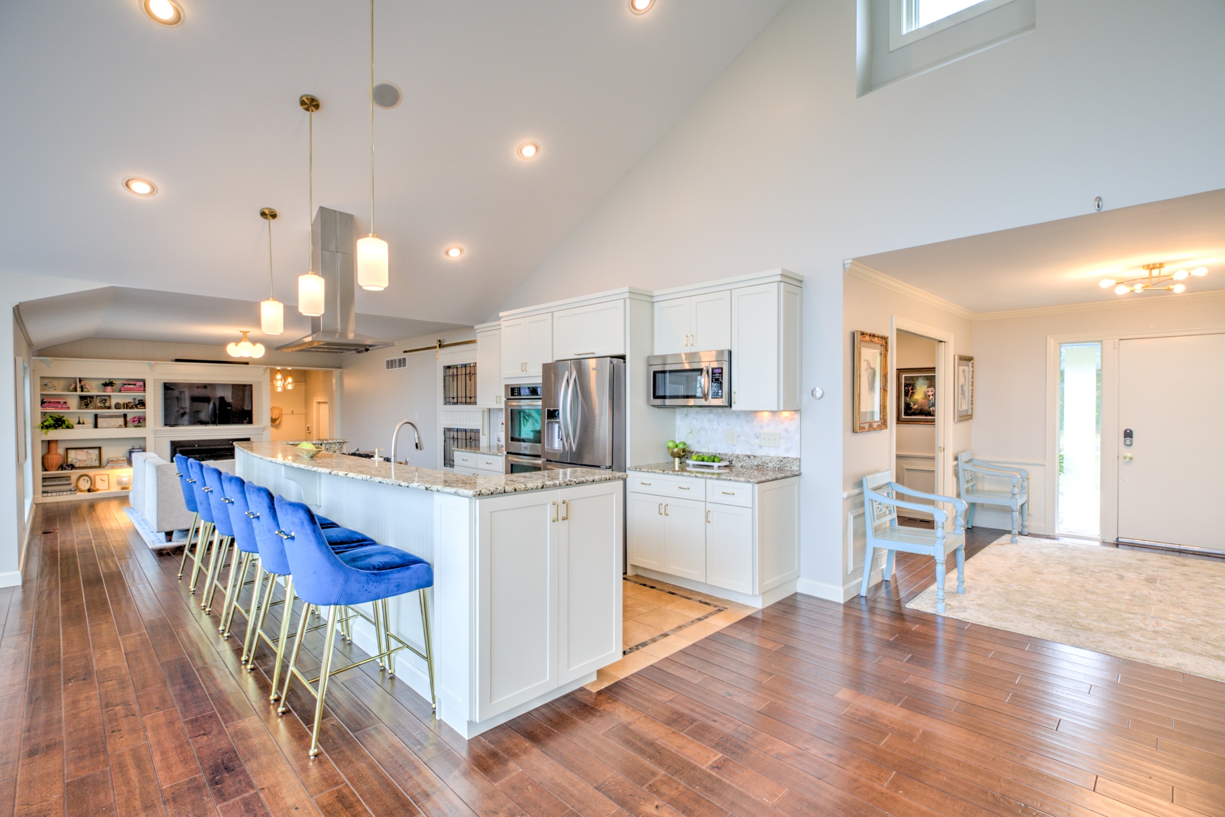 Bright open kitchen with a long granite island, blue velvet counter stools, white cabinetry, and adjoining living spaces