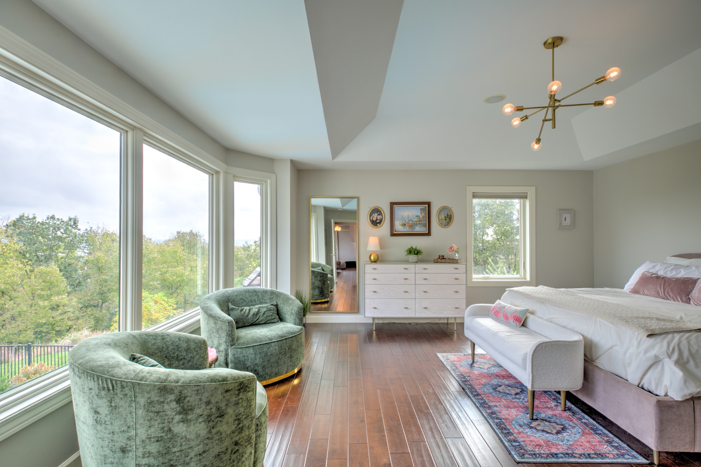 Spacious primary bedroom with large corner windows overlooking the wooded setting