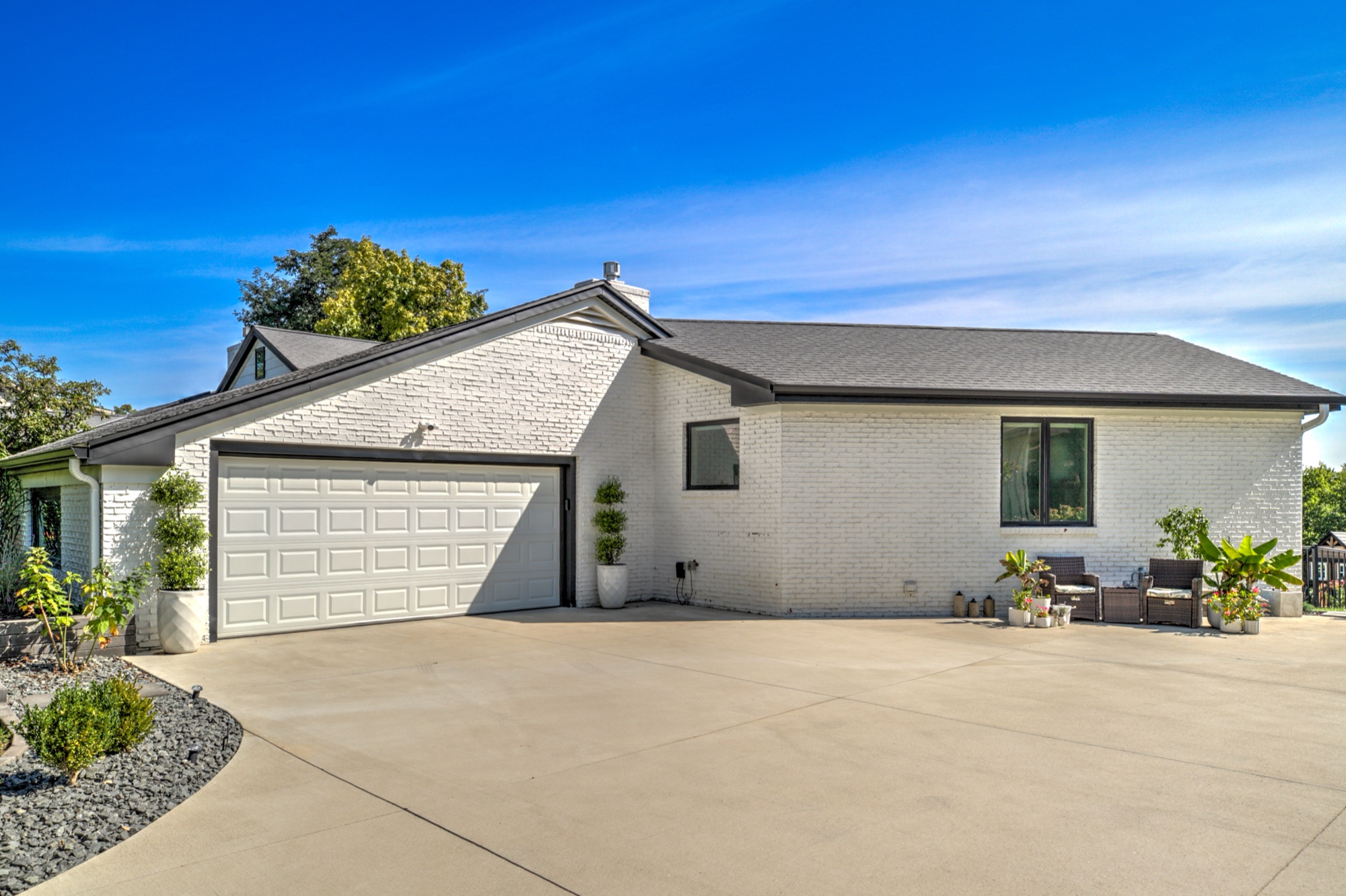 White brick side exterior, two car garage, broad driveway, and landscaped planting beds